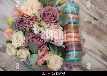 Bouquet de roses violettes et beiges, œillets roses, eustoma rose, freesia blanc et eucalyptus et macarons dessert français de différentes couleurs Banque D'Images