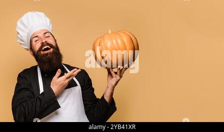 Homme barbu en uniforme de chef avec de la citrouille pour Halloween. Cuisine le jour de Thanksgiving. Manger végétarien sain. Recettes d'automne. Cuisinier homme dans le chapeau de chef avec Banque D'Images