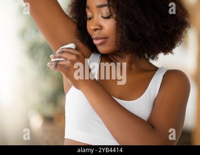 Magnifique femme noire utilisant l'épilateur pour éliminer les poils indésirables son aisselle à la maison Banque D'Images