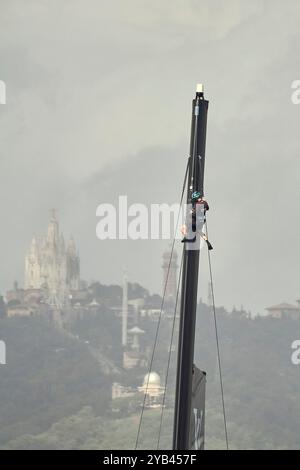 Barcelone, Espagne, 16/10/2024, 2024 America's Cup - Barcelone, Espagne Round Robin race 5-6 AC37 : Emirates Team New Zealand : comme les autres jours, les noirs ne laissent aucun détail désélectionné, donc encore un homme sur le mât, cette fois de l'intérieur du port le panorama derrière si l'Observatori Fabra et Tibidabo avec l'église Sagrat Cor et la Torre de les Aigües de dos Rius. CRÉDIT PHOTO : © Alexander Panzeri/PPL Banque D'Images