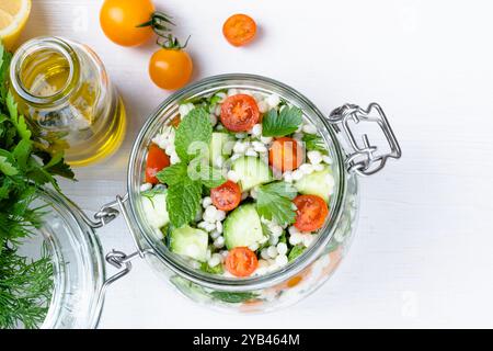 Salade de couscous frais dans un pot en verre avec concombres, tomates, herbes, citron avec des ingrédients sur fond blanc. Salade de taboulé. Végétarien en bonne santé Banque D'Images