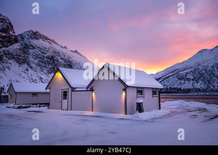 Lever de soleil sur les chalets norvégiens et les montagnes enneigées à Torsken sur l'île de Senja, Norvège en hiver. Paysage d'hiver avec chaîne de montagnes enneigée Banque D'Images