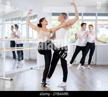 Heureuse femme souriante habillée en vêtements de sport noir et blanc appréciant la chorégraphie de ballet avec un partenaire masculin pendant la classe de groupe dans le salon de danse Banque D'Images