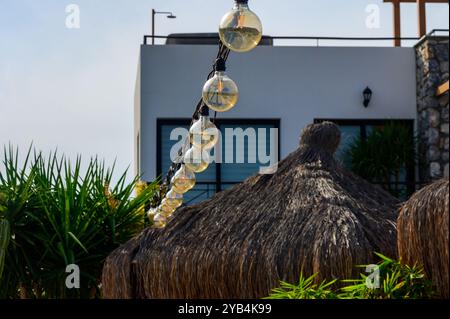 Des lanternes colorées sont suspendues au-dessus d'un jardin luxuriant avec toiture de chaume et plantes tropicales, créant une atmosphère chaleureuse et accueillante parfaite pour se détendre Banque D'Images