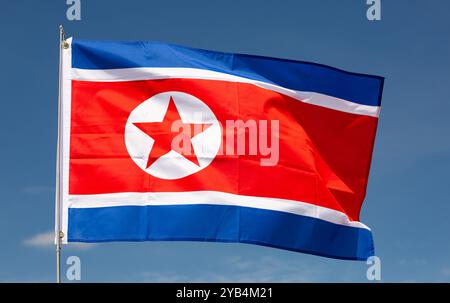 Sur fond de ciel bleu, le drapeau de la Corée du Nord bat sur le mât de drapeau Banque D'Images