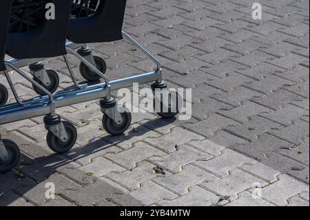 Une rangée de chariots se trouve sur un trottoir pavé, avec leurs roues projetant des ombres dans la lumière du soleil. Le quartier reflète une atmosphère commerçante animée. Banque D'Images