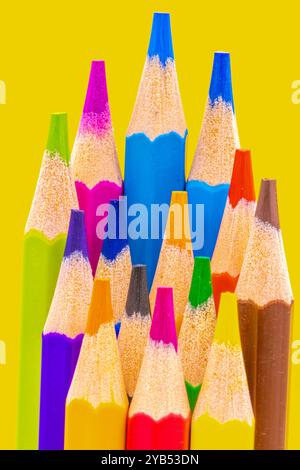 Cette image montre un gros plan d'une collection de crayons colorés et aiguisés disposés sur un fond jaune vif. Banque D'Images