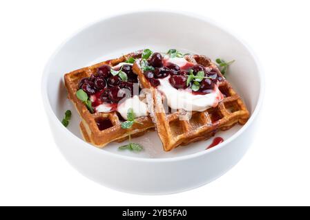 Assiette blanche avec gaufres belges sucrées avec de la crème et de la confiture de cerises sur un fond blanc assiette blanche avec des gaufres belges sucrées avec de la crème et de la confiture de cerises Banque D'Images