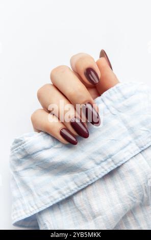 La main d'une femme présente une élégante manucure rouge foncé, avec de longs ongles pointus parfaitement polis. La main repose sur un tissu bleu doux, créant un sty Banque D'Images