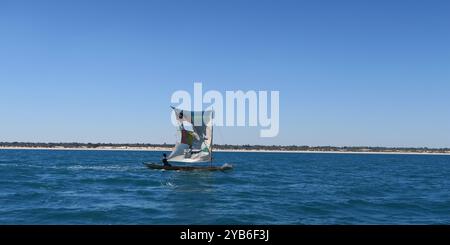 Petit bateau de pêcheur Pirogue avec voile arrachée quittant la côte ouest de Madagascar pendant la matinée près de Belo sur mer. Banque D'Images