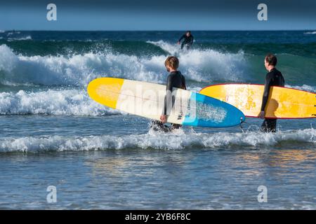 Surfeurs marchant dans la mer avec leurs planches de surf colorées à Fistral à Newquay en Cornouailles au Royaume-Uni en Europe Banque D'Images