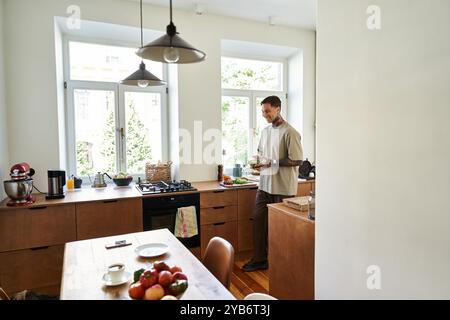 Dans une cuisine chic, un jeune homme cuisine un repas avec des ingrédients frais, savourant le moment. Banque D'Images