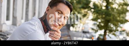 Dans un cadre de maison confortable, un jeune homme sourit joyeusement tout en se reposant pendant les heures de lumière du jour. Banque D'Images
