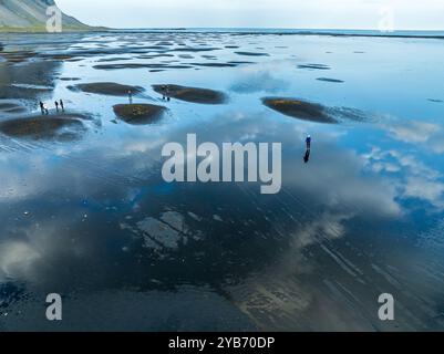 Vue aérienne de la plage de lave noire à Mt. Vestrahorn, les gens sur la plage, les nuages se reflètent sur l'eau, Stokksnes, à l'est de Höfn, Fjords est, Icel Banque D'Images
