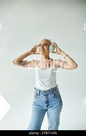 Une jeune femme chauve atteinte d'alopécie danse joyeusement, portant de grands écouteurs dans un studio élégant. Banque D'Images