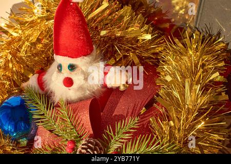 Jouet en peluche du Père Noël assis au milieu d'une scène de Noël festive. La figure du Père Noël, avec sa barbe blanche moelleuse, son costume rouge vif et ses yeux bleus, est surr Banque D'Images