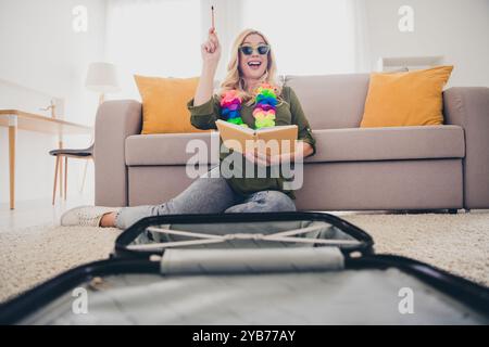 Photo de femme folle excitée assise sur le sol écrivant des plans pour la visite du week-end organisant valise à l'intérieur appartement plat Banque D'Images