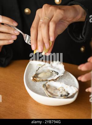 Une personne versant du jus de citron sur des huîtres de haute qualité Banque D'Images