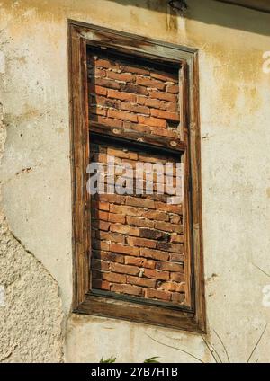 Maison abandonnée : ancien cadre de fenêtre en bois barricadé de briques Banque D'Images