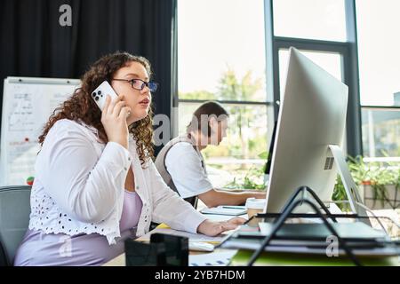 Une jeune femme de grande taille parle au téléphone, collaborant avec son amie dans un espace de travail dynamique. Banque D'Images