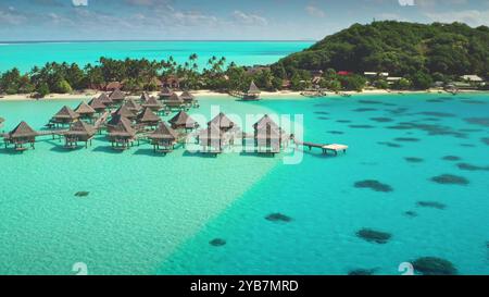 Bungalows de luxe sur l'eau dans un lagon cristallin turquoise avec plage de sable de l'île tropicale en arrière-plan. Vue aérienne de drone de vacances de luxe exotiques parfaites de voyage d'été. Fond de nature sauvage Banque D'Images