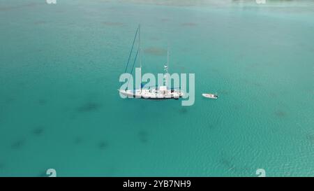 Vue aérienne du voilier yacht avec dinghy ancré dans le lagon océanique turquoise d'eau claire. Paradis de la nature sauvage à distance, voyage de luxe exotique d'été, concept de vacances. Panorama de tir par drone Banque D'Images