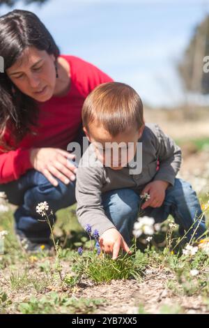 Une femme et un enfant regardent des fleurs dans un champ. L'enfant cherche une fleur et la femme s'agenouille pour l'aider. La scène est pe Banque D'Images