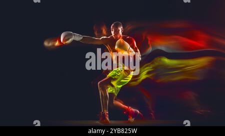 Boxeur masculin concentré en mouvement jetant un puissant punch, portant un short vert vif et des gants blancs. Fond sombre avec effet de lumière mixte. Banque D'Images