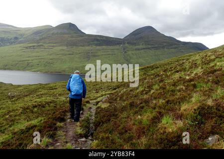 Homme solitaire (randonneur) marchant jusqu'au Loch Eilde Mor depuis la montagne écossaise Corbett 'Glas Bheinn' dans les Highlands écossais, Écosse Royaume-Uni. Banque D'Images