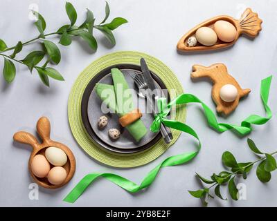 Vue d'en haut de la table de Pâques. Cadre de vacances aux couleurs naturelles. Assiettes rondes et figurées, serviettes et ruban verts, œufs bio, couverts, printemps Banque D'Images