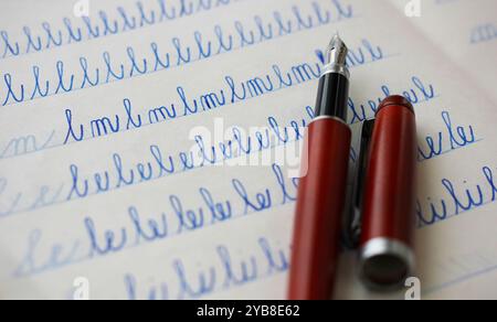 Gros plan d'un stylo plume Bordeaux et de lettres bleues écrites en cursive par un enfant dans un cahier en papier Banque D'Images