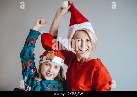 Mère et fille portant des chapeaux de Père Noël, moment de Noël ludique, amusement de vacances, liens familiaux, esprit festif, joyeuse célébration. Banque D'Images