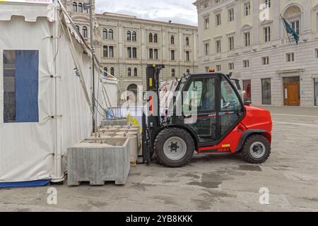 Trieste, Italie - 08 octobre 2024 : chariot élévateur diesel Manitou soulevant des poids en béton pour la tente de canopée pop up à la place de la ville. Banque D'Images