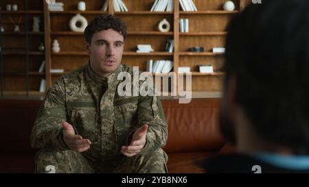 Inquiet nerveux caucasien officier homme vétéran soldat militaire de l'armée homme Guy dans le camouflage de combat assis canapé salle de thérapie intérieure parlant le partage Banque D'Images