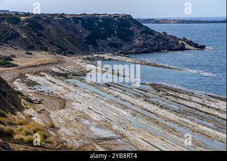 Le rivage présente des formations rocheuses frappantes exposées à marée basse, avec de douces vagues qui rodent contre les falaises accidentées et un ciel bleu vif Banque D'Images
