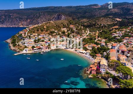 Vue aérienne d'Assos, Céphalonie. Village pittoresque niché sur une péninsule, entouré d'eaux turquoises. Maisons colorées, petite plage et bateaux i Banque D'Images