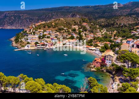 Vue aérienne d'Assos, Céphalonie. Village pittoresque niché sur une péninsule, entouré d'eaux turquoises. Maisons colorées, petite plage et bateaux i Banque D'Images