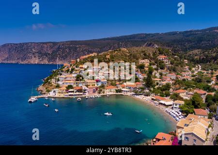 Vue aérienne d'Assos, Céphalonie. Village pittoresque niché sur une péninsule, entouré d'eaux turquoises. Maisons colorées, petite plage et bateaux i Banque D'Images