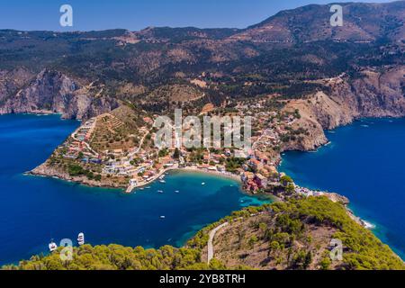 Vue aérienne d'Assos, Céphalonie. Village pittoresque niché sur une péninsule, entouré d'eaux turquoises. Maisons colorées, petite plage et bateaux i Banque D'Images