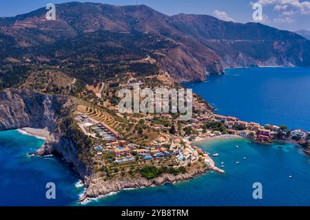 Vue aérienne d'Assos, Céphalonie. Village pittoresque niché sur une péninsule, entouré d'eaux turquoises. Maisons colorées, petite plage et bateaux i Banque D'Images