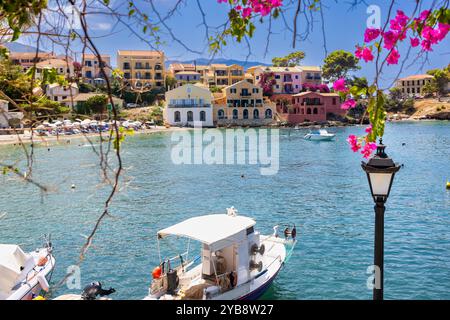 Un village pittoresque à Assos, Céphalonie, Grèce. Des maisons colorées bordent la côte avec un petit port et des bateaux. L'image est encadrée par un b rose vif Banque D'Images