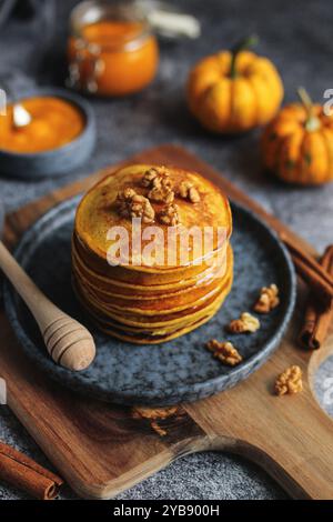 Crêpes de citrouille légères et moelleuses avec miel et noix sur une assiette bleue. Planche à découper en bois, citrouille pure dans un pot en verre, bâtonnets de cannelle, et sombre Banque D'Images