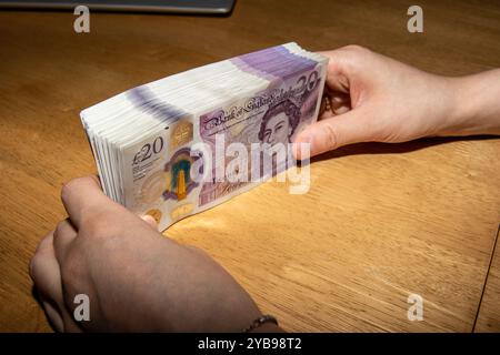 Une personne tenant une pile de billets britanniques de vingt livres sur une table en bois. Les notes sont soigneusement arrangées, mettant en valeur leur couleur violette et distinguc Banque D'Images