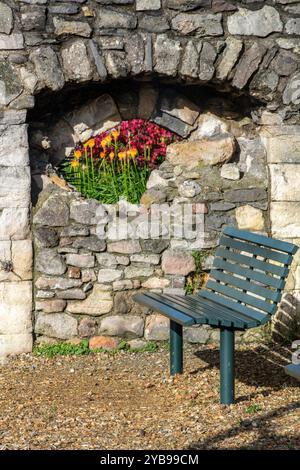 Banc vide à côté des vieux murs médiévaux marcher à Southampton, Hampshire, Royaume-Uni avec un jardin de fleurs visible à travers un trou dans les murs d'origine en pierre Banque D'Images