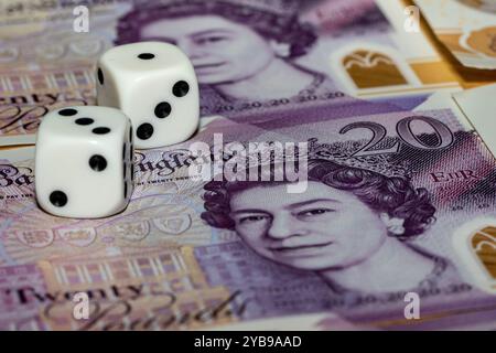Deux dés blancs avec des points noirs reposent sur un billet de vingt livres mettant en vedette la reine Elizabeth II. le billet est partiellement visible, montrant la dénomination et le s. Banque D'Images