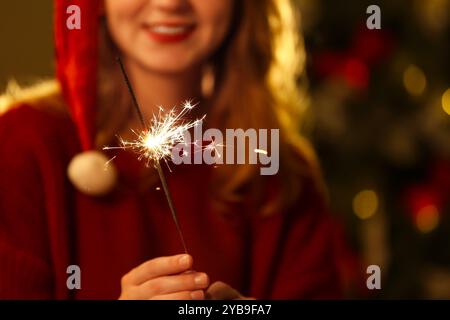 Femme joyeuse dans le chapeau de Santa célébrant Noël avec Sparkler sur fond de lumières floues Banque D'Images