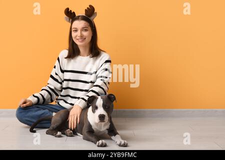 Jeune femme dans des cornes de renne avec chiot Staffordshire Terrier mignon près du mur jaune Banque D'Images