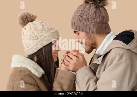 Couple aimant dans les vêtements d'hiver réchauffant les mains sur fond beige, gros plan Banque D'Images