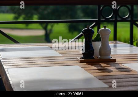 Une table à manger magnifiquement agencée attend les invités, affichant des sauterelles de sel et de poivre noir et blanc sur une surface en bois. Un parcours de golf serein ajoute un Banque D'Images