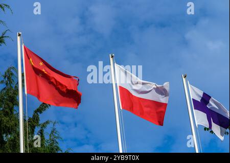 Trois drapeaux s'élèvent contre un ciel bleu clair, rouge vif pour la Chine, blanc et rouge pour la Pologne et bleu et blanc pour la Finlande, incarnant l'unité et la culture Banque D'Images